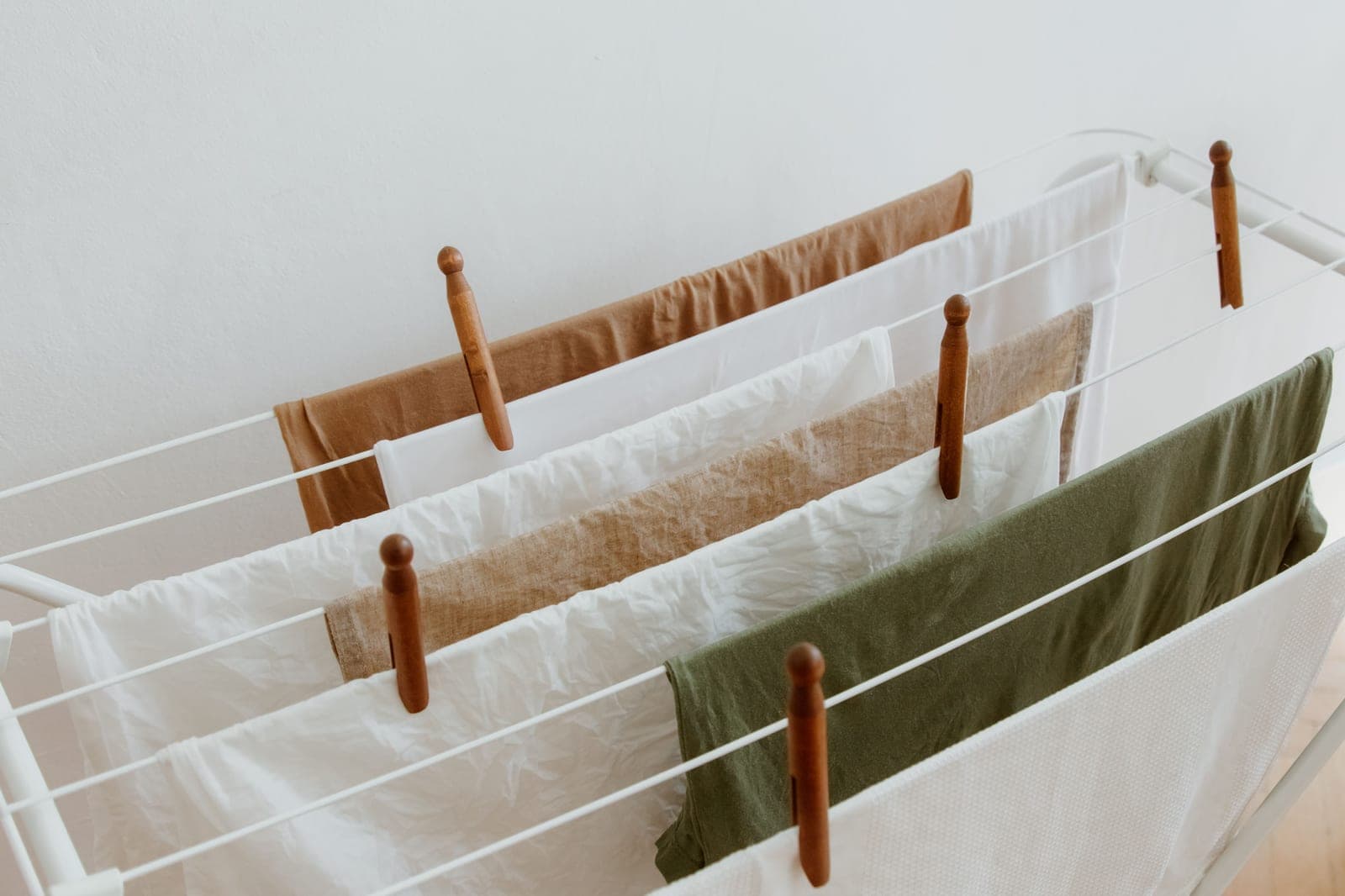 A white folding clothes airer hung with laundry and wooden pegs against a white wall