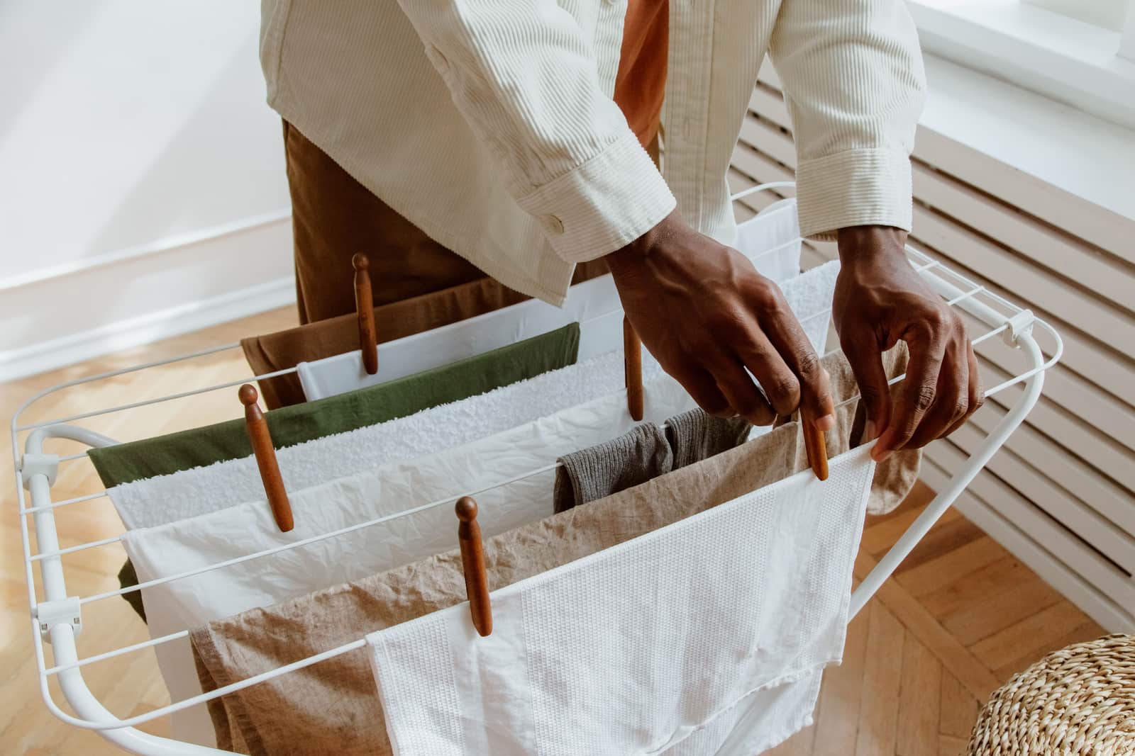 A white folding laundry drying rack standing beside a window