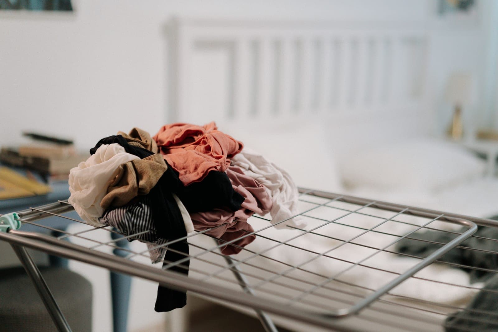 A metal clothes drying rack loaded with laundry in a bright bedroom